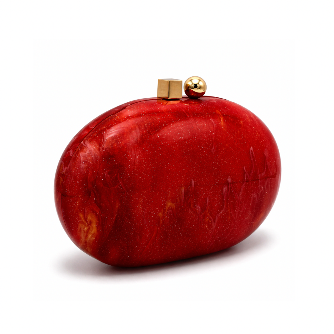 L’APOGÉE Rubelle oval acrylic clutch featuring glossy ruby red marbled textures, a smooth sculptural silhouette, and gold metallic clasp detailing designed for glamorous evening styling and statement party looks.