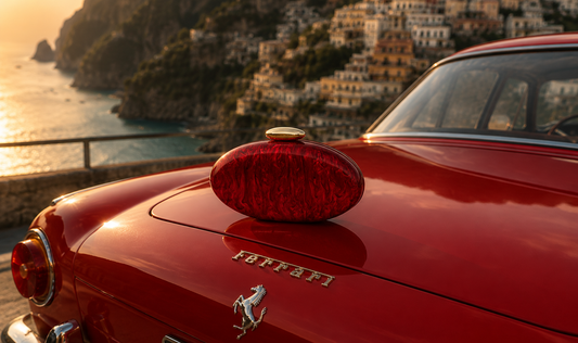 Rouge Éclat red acrylic clutch by L’APOGÉE displayed on a vintage red Ferrari overlooking the Amalfi Coast at sunset.