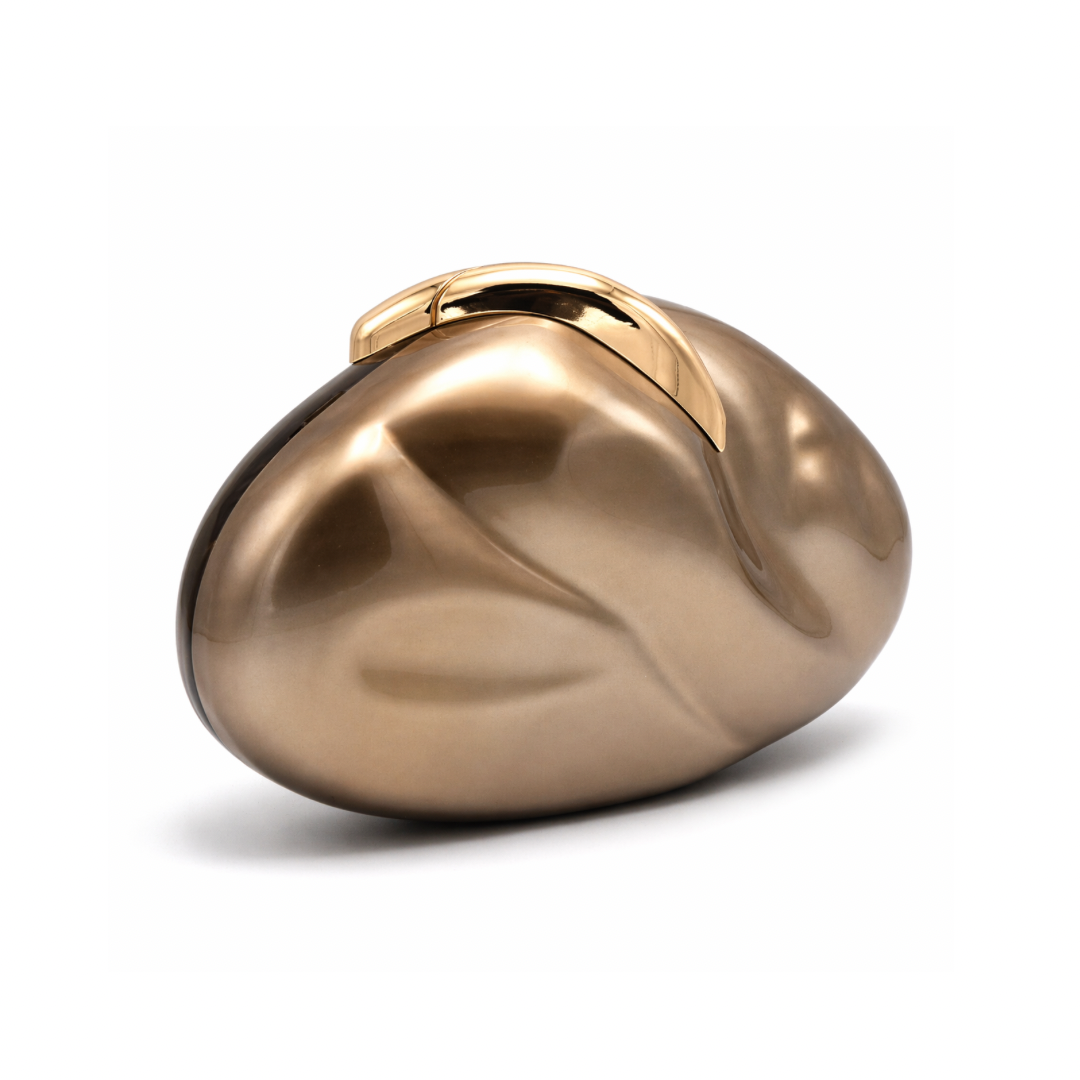 L’APOGÉE Sovana in Brown acrylic clutch featuring warm caramel brown marbled tones, a smooth pebble-inspired silhouette, and sculptural gold metallic handle designed for chic dinner parties and sophisticated evening styling.