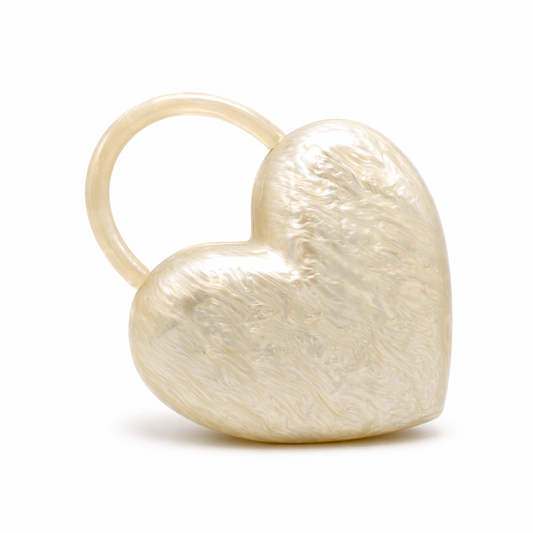 L’APOGÉE Amouré sculptural heart-shaped acrylic clutch featuring pearly ivory textures and an integrated circular handle designed for romantic evening styling, bridal looks, and statement fashion moments.