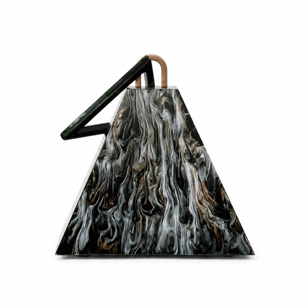 L’APOGÉE Nefra pyramid-shaped acrylic clutch featuring glossy black marbled textures, an architectural geometric silhouette, and a sculptural triangular handle designed for bold evening styling and avant garde luxury fashion looks.