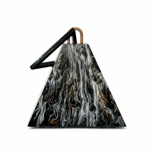 L’APOGÉE Nefra pyramid-shaped acrylic clutch featuring glossy black marbled textures, an architectural geometric silhouette, and a sculptural triangular handle designed for bold evening styling and avant garde luxury fashion looks.