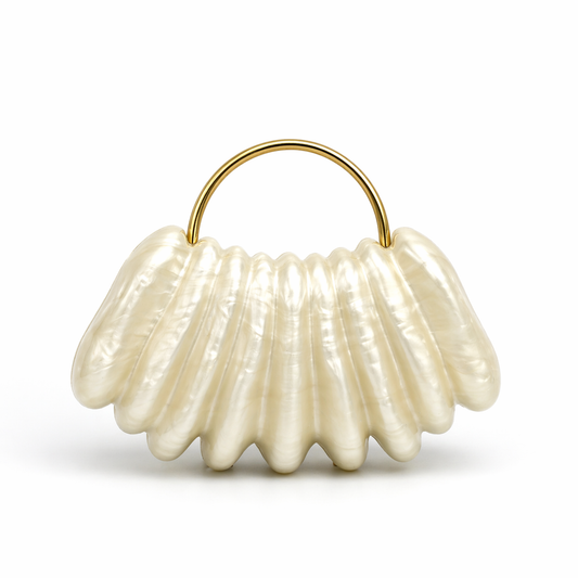 L’APOGÉE Ondée shell-inspired evening bag featuring pearly ivory finishes, sculptural ridged textures, and a sleek metallic top handle designed for bridal styling and elegant luxury fashion looks.