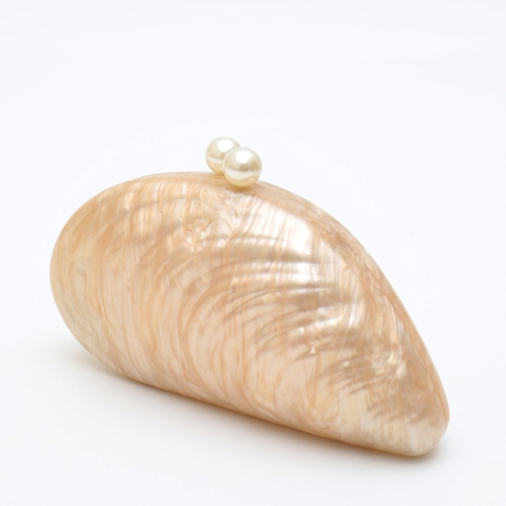 L’APOGÉE Elefteria beige shell-shaped evening bag featuring a sculptural glossy design for weddings, formal events, vacations, and elegant statement occasion styling.